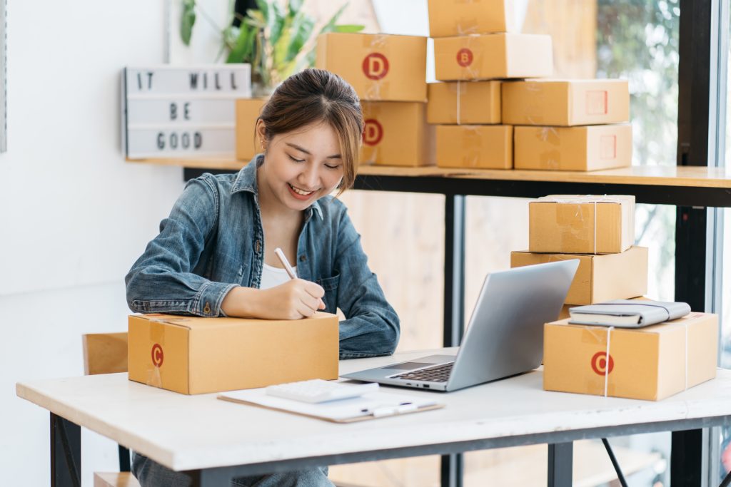 asian woman entrepreneur is packing product to the box at home w
